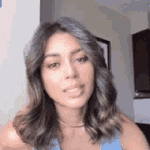 a woman with long brown hair is wearing a blue tank top and a choker necklace .