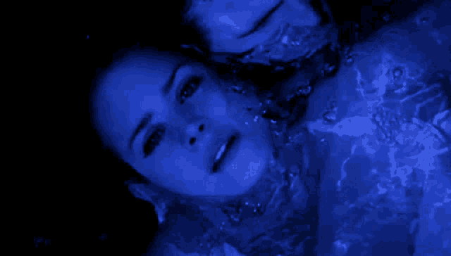 a woman is swimming in a pool with a blue light shining on her face