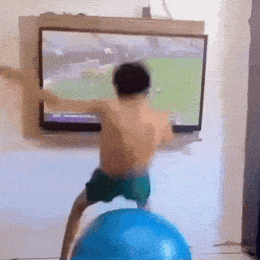 a young boy is standing on a blue exercise ball in front of a television .