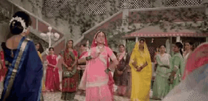 a woman in a pink dress is dancing in front of a group of women in traditional dresses .