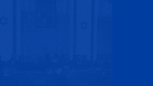 a group of men are sitting at a table with a man giving a speech and the word am is on the blue background