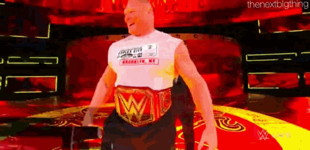 a man wearing a wrestling belt is standing on a stage with a red background .