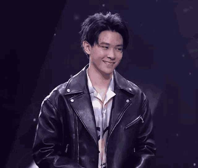 a young man wearing a black leather jacket smiles
