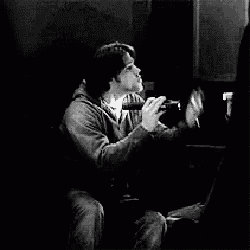 a black and white photo of a person sitting in a dark room with a light shining on them .