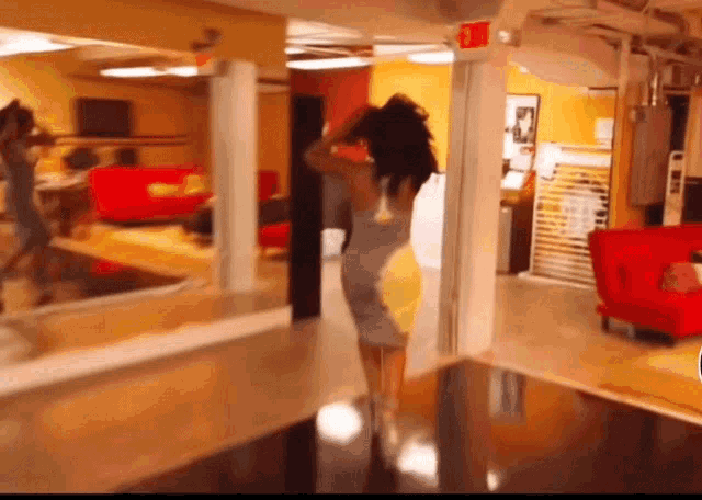 a woman in a grey and yellow dress is standing in a hallway next to a red exit sign