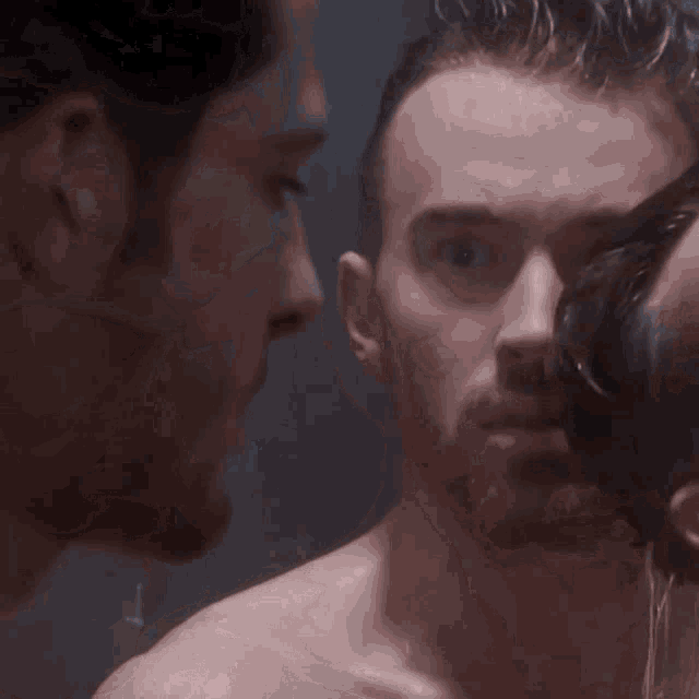 a man without a shirt is looking at another man in the mirror