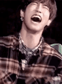 a young man in a plaid shirt is laughing with his mouth wide open .