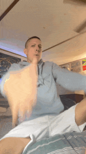 a man sitting on a bed with his arms outstretched wearing a light blue hoodie with a cartoon character on the front