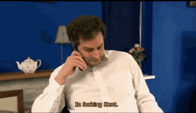 a man in a white shirt is talking on a cell phone and says " in fucking kent " at the bottom