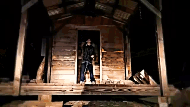 a man in a black jacket stands in front of a wooden building at night