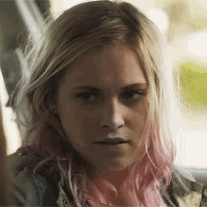 a woman with blonde hair and pink highlights looks at the camera