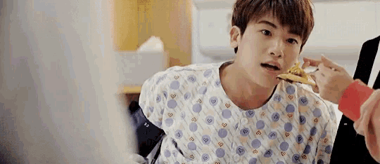 a young boy in a hospital gown is eating a slice of pizza .