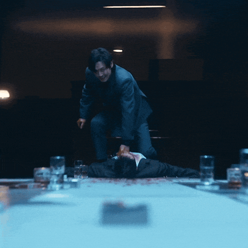 a man in a suit is standing over a man laying on the floor