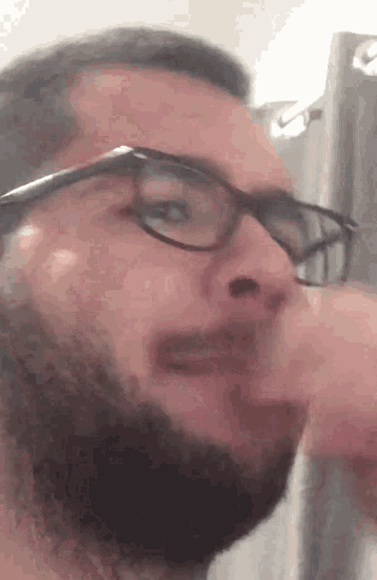 a man with a beard and glasses is looking at himself in a mirror .