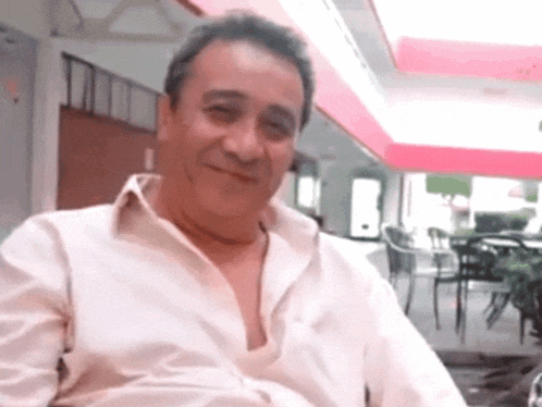 a man in a white shirt is sitting in a chair and smiling
