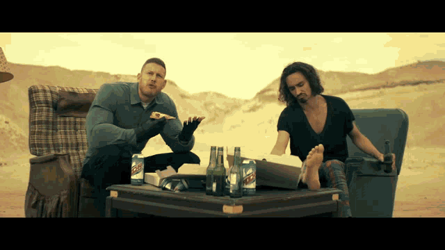 a man sitting on a couch eating a pizza next to a man sitting on a table with mtn dew cans
