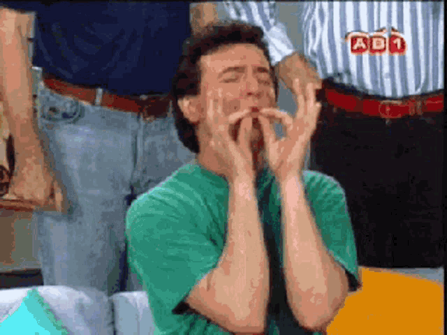a man in a green shirt is covering his mouth with his hands