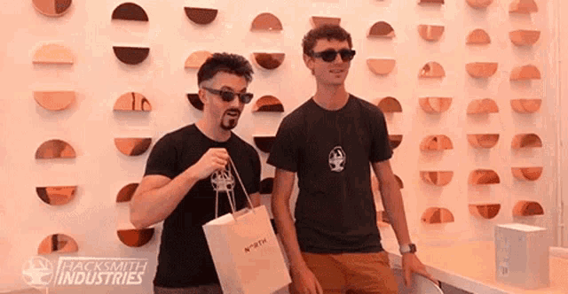 two men are standing in front of a wall that says hacksmith industries on it