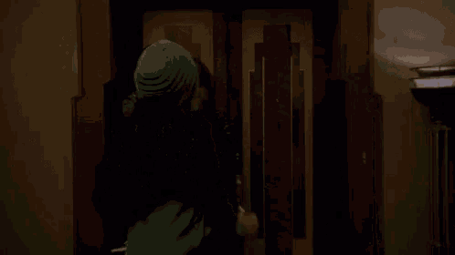 a woman in a green dress and a black fur coat is standing in a dark hallway .