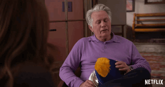 a man in a purple shirt is holding a hat and a netflix logo can be seen in the corner