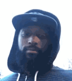 a man with a beard and a hat is wearing a hoodie .