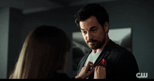 a woman in a leather jacket is holding a man 's arm with the cw logo on the bottom