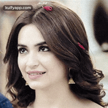 a woman with a flower in her hair is smiling and looking at the camera .