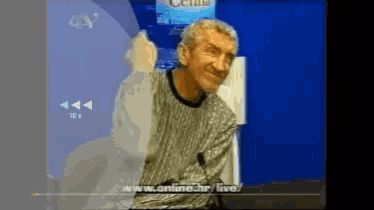 a man in a sweater is sitting in front of a screen that says online.hr/live