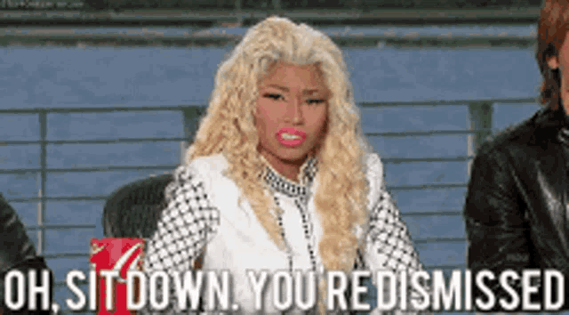 a woman with blonde hair is sitting in front of a sign that says oh sit down you redismissed