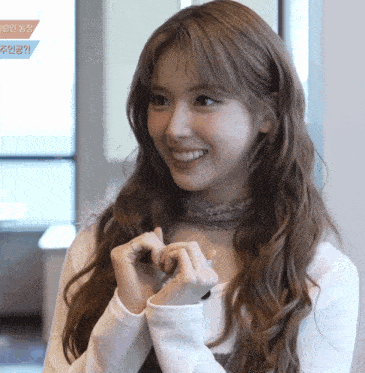 a woman making a heart shape with her hands with a foreign language on the bottom right