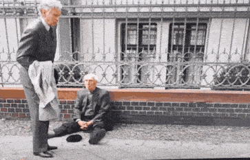a man in a suit is standing next to a man sitting on the ground