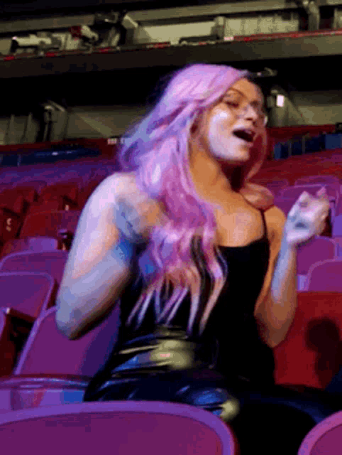 a woman with pink hair is sitting in a stadium with her mouth open .