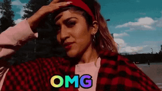 a woman wearing a red headband and a plaid jacket is taking a selfie and says omg .