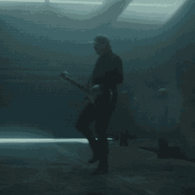 a man in a black hat is playing a guitar in a dark room
