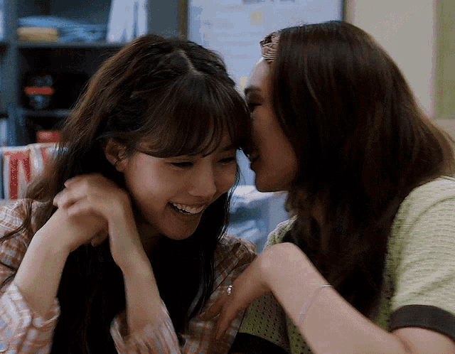 a woman whispers into another woman 's ear and they both smile
