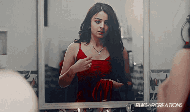 a woman in a red dress is looking at herself in a mirror with ruksarcreations written below her