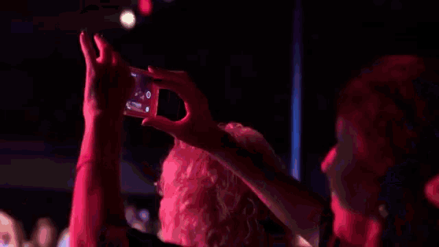 a woman taking a picture of a man in a dark room with purple lights