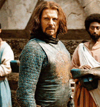 a man with long hair and a beard is wearing a blue shirt with a lion on it