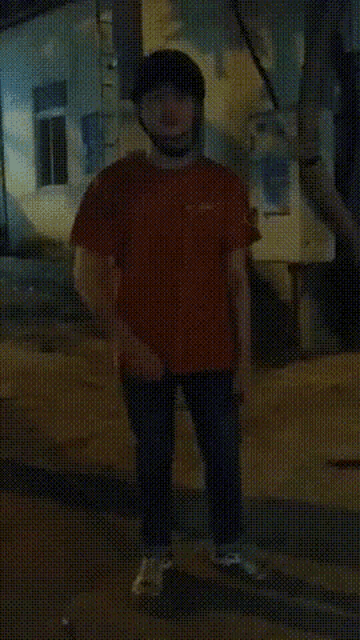 a man wearing a helmet and a red shirt is standing on a street at night