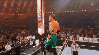 a wrestler is standing on a stage in front of a crowd while a referee watches .