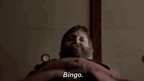 a man with a beard is laying on a bed and says bingo .