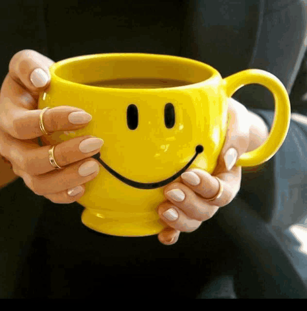 a woman holds a yellow mug with a smiley face on it