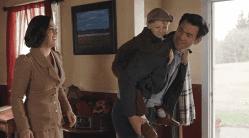 a man is carrying a child on his shoulders while a woman watches