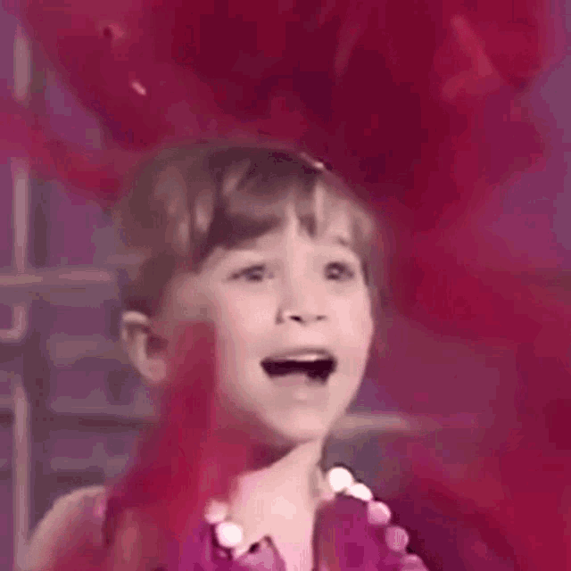 a little girl is standing in front of a red balloon and making a funny face .