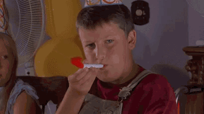 a young boy is brushing his teeth with a red toothbrush while a girl watches .