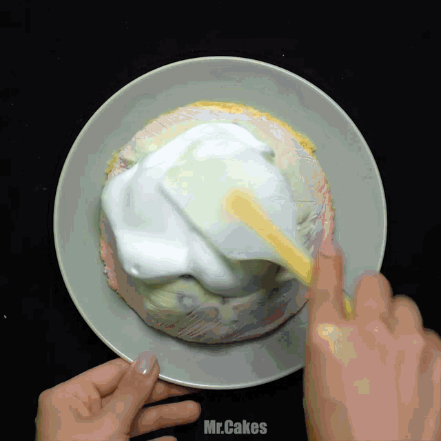 a person spreading whipped cream on top of a cake in a bowl with the words mr.cakes below it