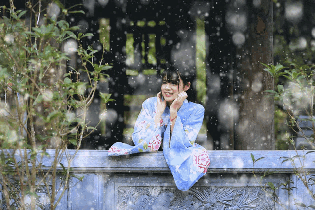 a woman in a blue kimono is leaning on a stone wall