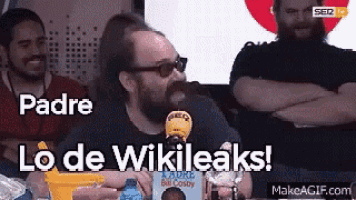 a man with a beard is sitting at a table with a microphone and says padre lo de wikileaks .