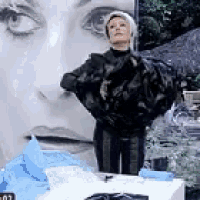 a woman in a black jacket is standing in front of a large picture of a woman 's face .