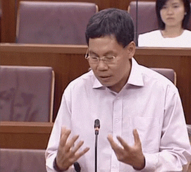 a man wearing glasses is speaking into a microphone in a classroom